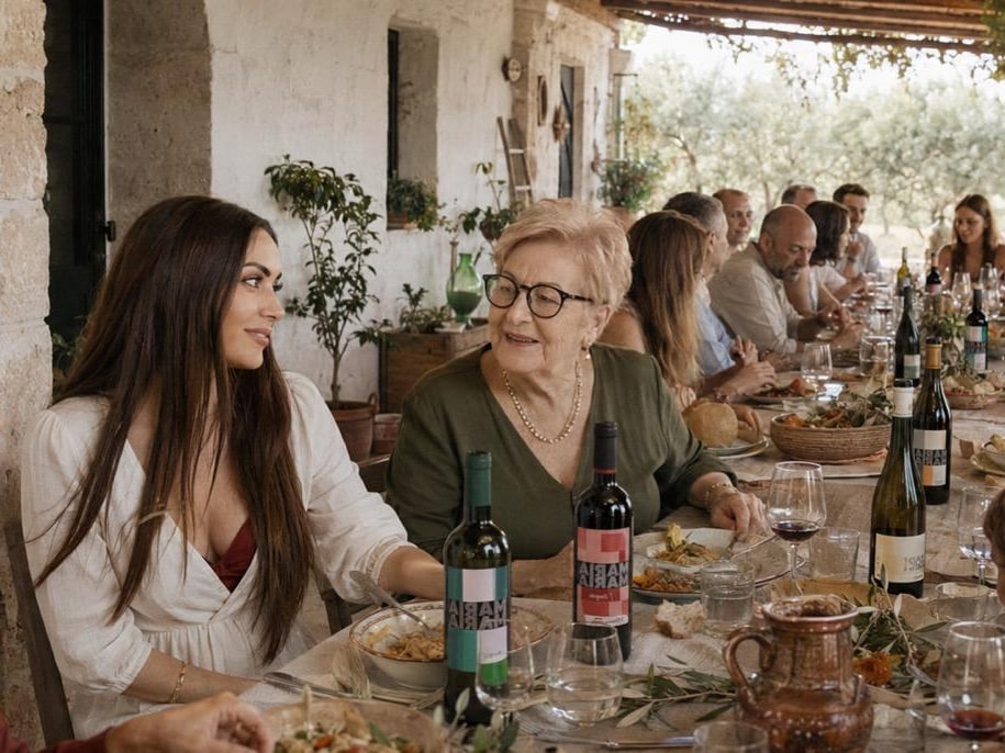 Zwei Generationen an einer langen Tafel unter der Pergola, davor zwei Flaschen Maria Maria